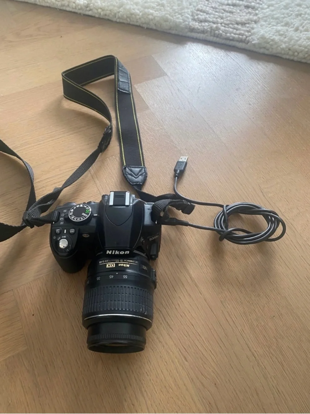 Nikon 3100 black DSLR with zoom lens and attached USB cable